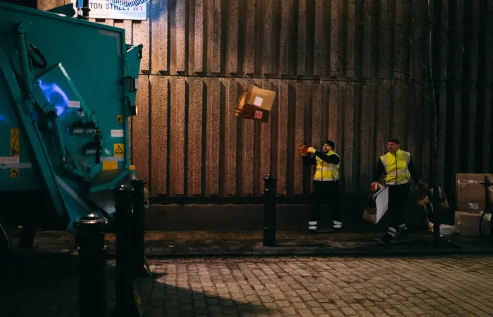 Unos trabajadores cargando un camión de basura con varios objetos.